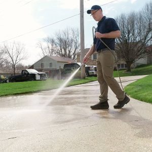 pressure washing professional in brown pants and blue shirt pressure washing concrete