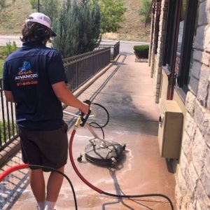 Advanced Window Cleaning professionals pressure washing commercial concrete in blue shirt and hat