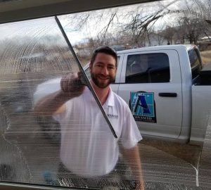 Advanced Window Cleaning professional in white shirt cleaning window with white work truck behind him